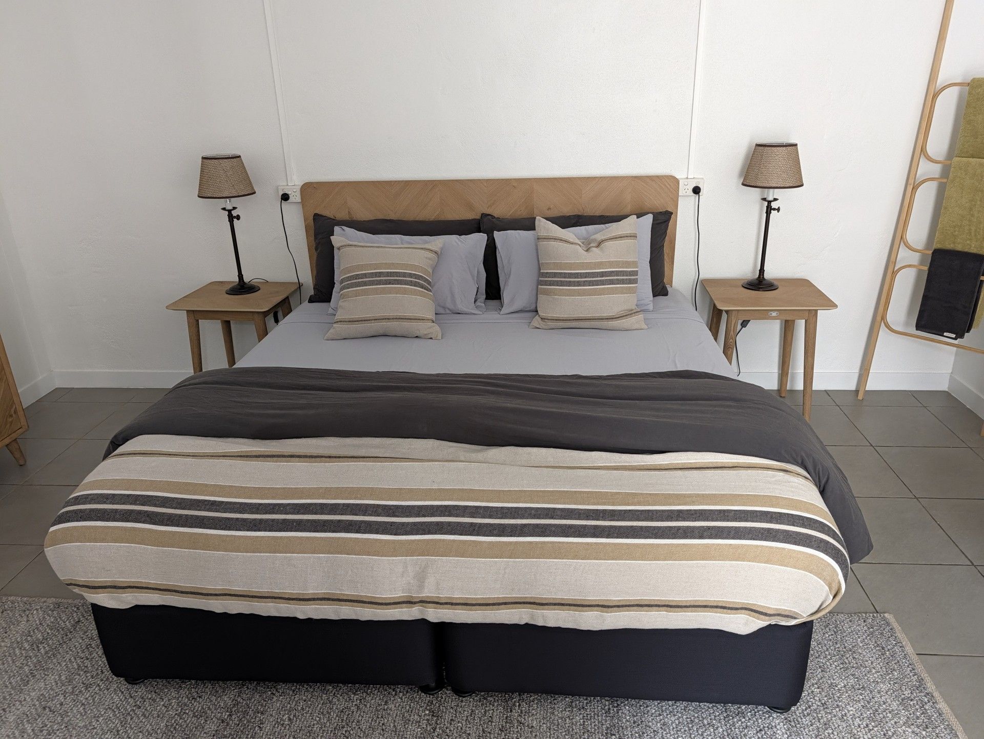 A neatly made bed with a striped blanket, two bedside tables with lamps, and a wooden headboard.