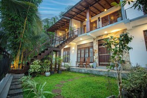 Una casa de dos pisos con una escalera de madera, un balcón y un jardín bien cuidado.