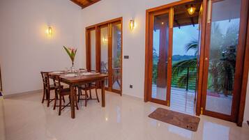 Comedor con mesa de madera dispuesta para cuatro, un florero con flores y vista a un jardín a través de puertas de cristal.