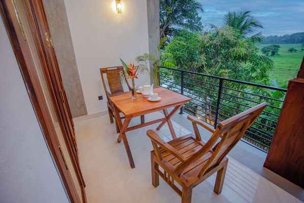 A wooden dining table with chairs and a vase of flowers on a balcony with a view of a green landscape.