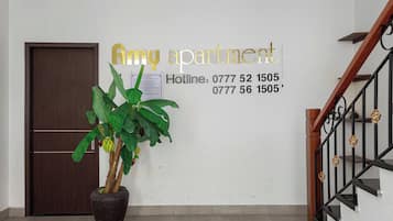 Un muro con il testo 'Amy apartment' e due numeri di telefono. Si nota una pianta in vaso con foglie verdi e una porta in legno sullo sfondo.