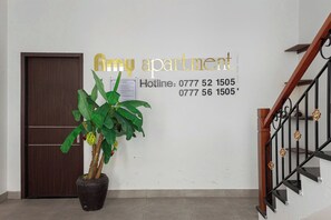 Un muro con il testo 'Amy apartment' e due numeri di telefono. Si nota una pianta in vaso con foglie verdi e una porta in legno sullo sfondo.