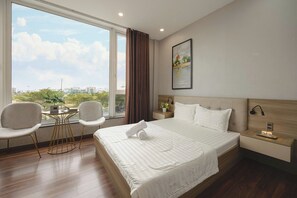 A hotel room with a large window, a bed with white linens, two chairs, a bedside table with a lamp, and a painting on the wall. - Amy Apartment Hue  (An Dong)