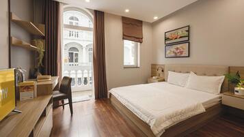 Habitación de hotel con una cama grande, un escritorio con silla, una ventana con cortinas y una obra de arte en la pared.