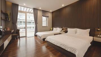 A hotel room with a wooden floor, two beds, a desk, a chair, a TV, and a balcony with curtains.