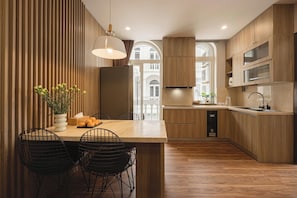 A modern kitchen with wooden cabinets, a central island with seating, and a view of a building through a window.