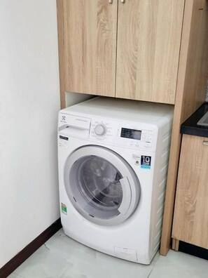 A front-loading washing machine in a corner with wooden cabinets above.