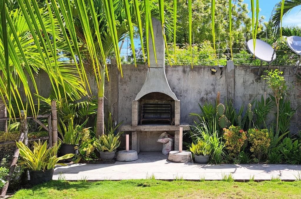 Un espacio exterior con una estructura de concreto, posiblemente una parrilla o barbacoa, rodeado de plantas en macetas y follaje variado.
