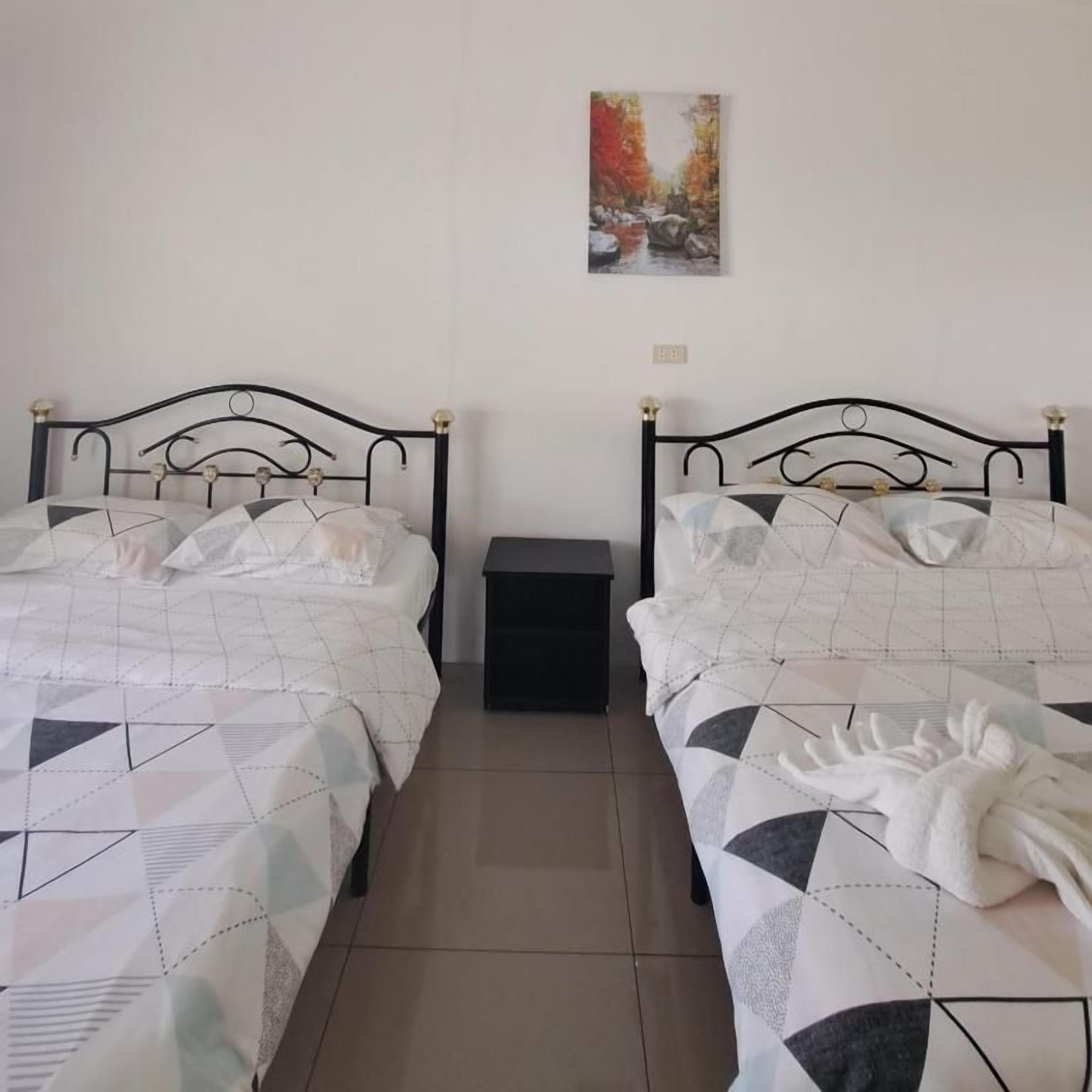 Un dormitorio con dos camas, cada una con colcha de estampado geométrico, una mesita de noche pequeña y un cuadro colgado en la pared.