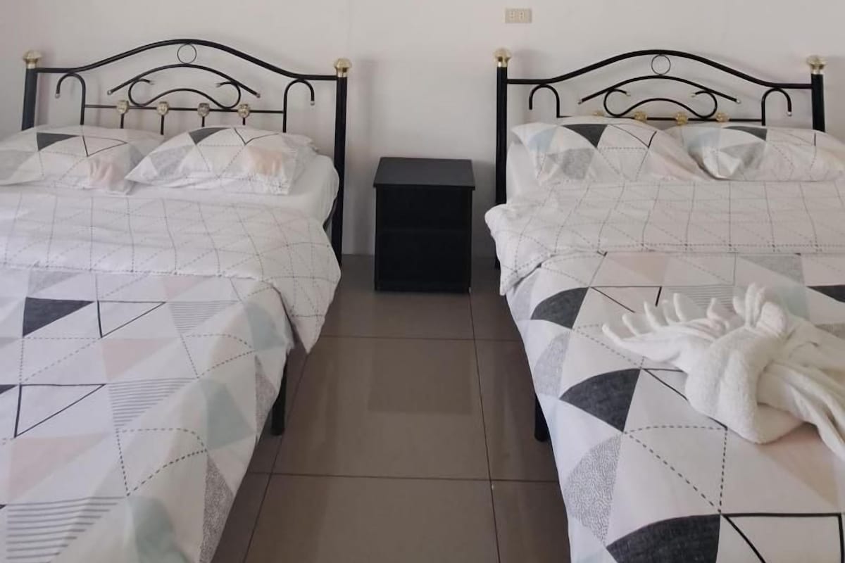 A bedroom with two beds, each with a geometric-patterned bedspread, a small bedside table, and a wall-mounted picture.