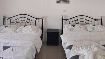 Un dormitorio con dos camas, cada una con colcha de estampado geométrico, una mesita de noche pequeña y un cuadro colgado en la pared.