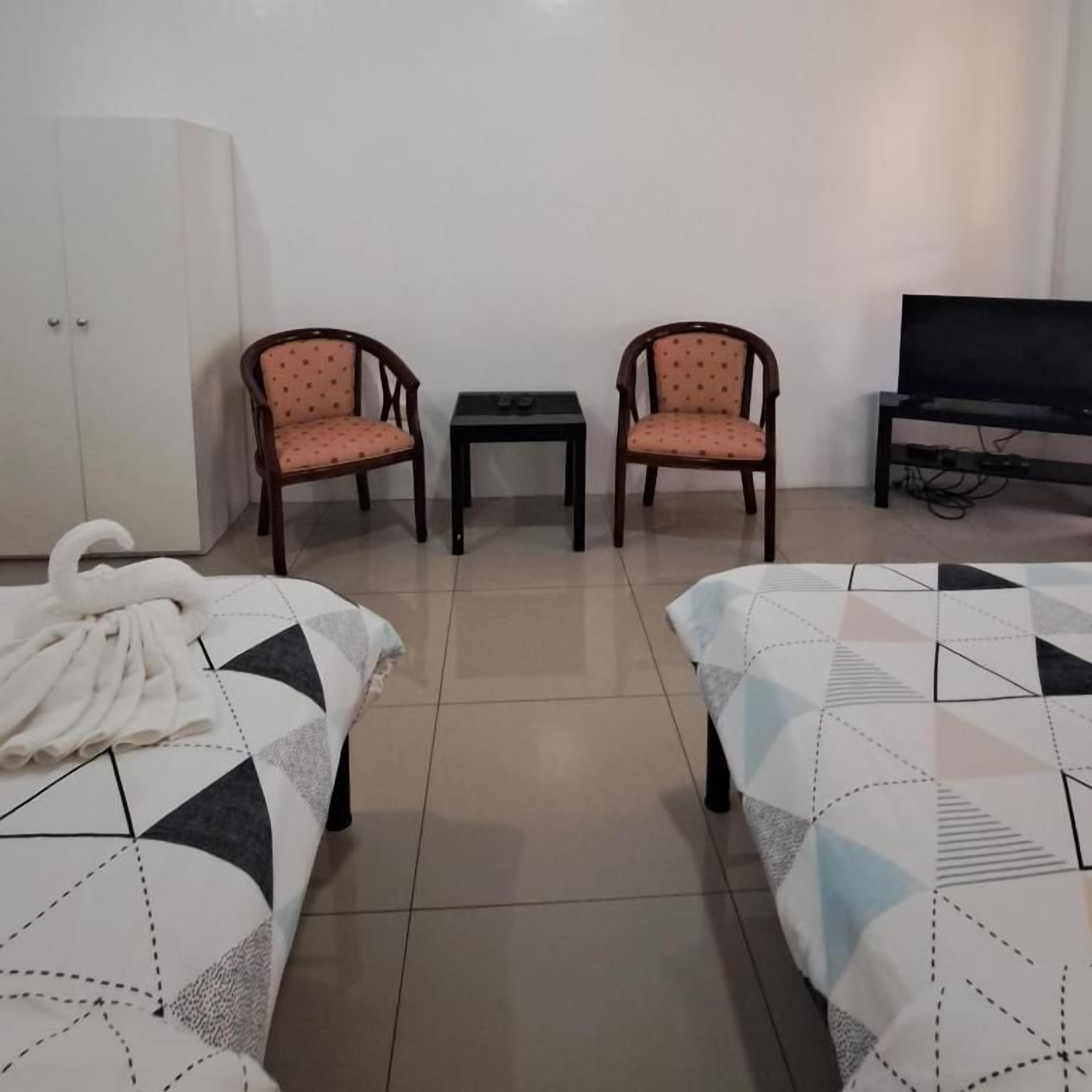 A hotel room with two beds, a TV, a wardrobe, and two chairs.