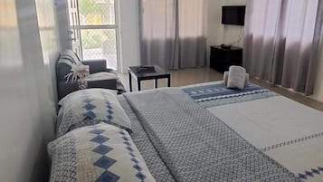 Habitación de hotel con cama, escritorio, silla, televisor y ventana con cortinas.