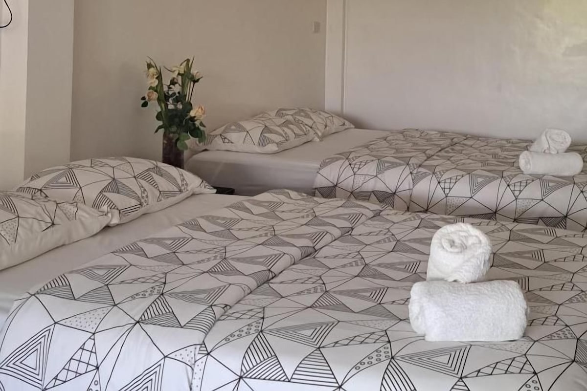 A hotel room with two beds, a painting of a beach scene, and a vase with flowers.