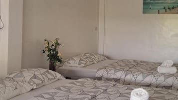 A hotel room with two beds, a painting of a beach scene, and a vase with flowers.