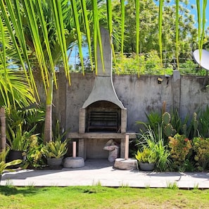 A concrete outdoor area with a built-in grill, surrounded by various potted plants and greenery.