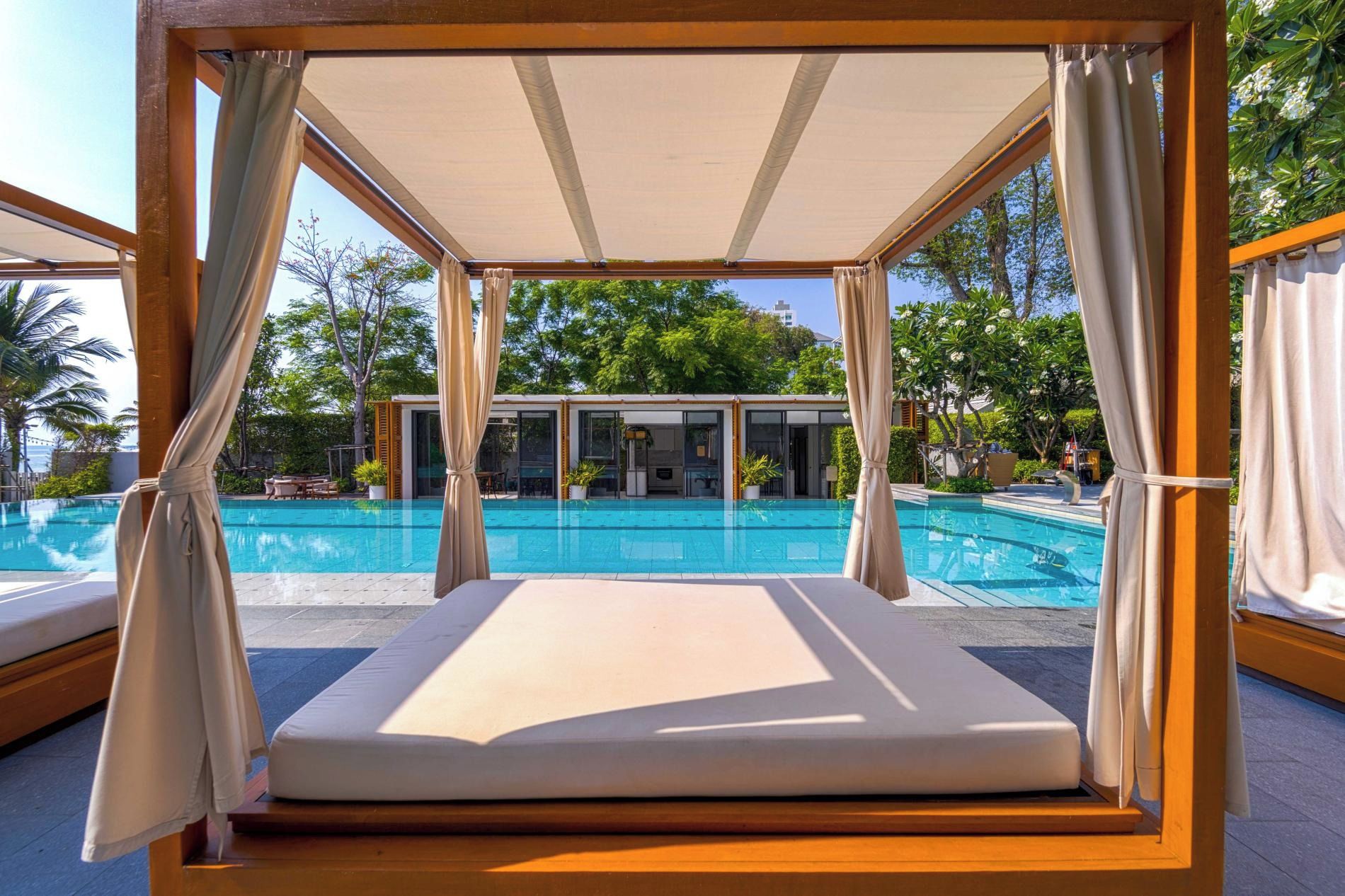 Un salon au bord de la piscine, doté d’un espace salon avec des sièges confortables, d’une piscine et d’un bâtiment en arrière-plan.