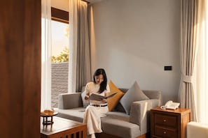 Una persona sentada en un sofá en una habitación con una mesa de madera, un teléfono y una ventana con cortinas.