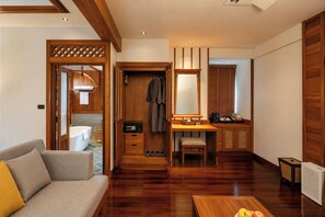 Habitación de hotel moderna con piso de madera, un sofá, un escritorio con espejo y un baño visible a través de una puerta abierta.