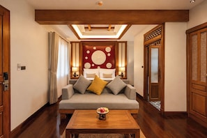 Habitación de hotel con sofá, mesa de centro de madera y cama con pared decorada en rojo.