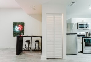 Eine moderne Küche mit integriertem Mikrowellenherd, Backofen und einem weißen Schrank. Es gibt eine Bar mit Hockern und ein Neon-Schild an der Wand.