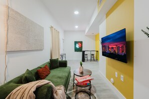 Ein modernes Wohnzimmer mit einem grünen Sofa, einem Couchtisch mit Gesellschaftsspielen, einem Flachbildfernseher und einem Stadtbild.