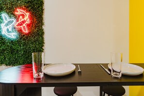 Une table à manger avec deux assiettes, une fourchette et un verre, placée devant un mur orné d'un décor texturé vert et d'un panneau lumineux au néon.