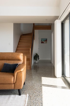 A modern interior with a wooden staircase, a leather sofa, and a potted plant. - Timbre Blue - Want for nothing (Break O'Day)