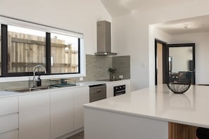 Une cuisine moderne avec des meubles blancs, une hotte en acier inoxydable et une grande fenêtre.