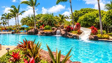 A pool with a waterfall, surrounded by palm trees and tropical plants.