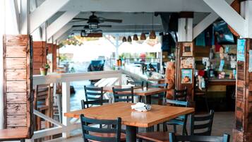 An indoor dining area with wooden tables and chairs, a counter with menu boards, and a view of the outdoors.