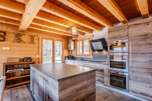 A modern kitchen with wooden beams, a large island, stainless steel appliances, and a view of the outdoors. - Chalet Cerf, Sleeps 10, Hot Tub, Ascension Immobilier (LA COTE D ARBROZ)
