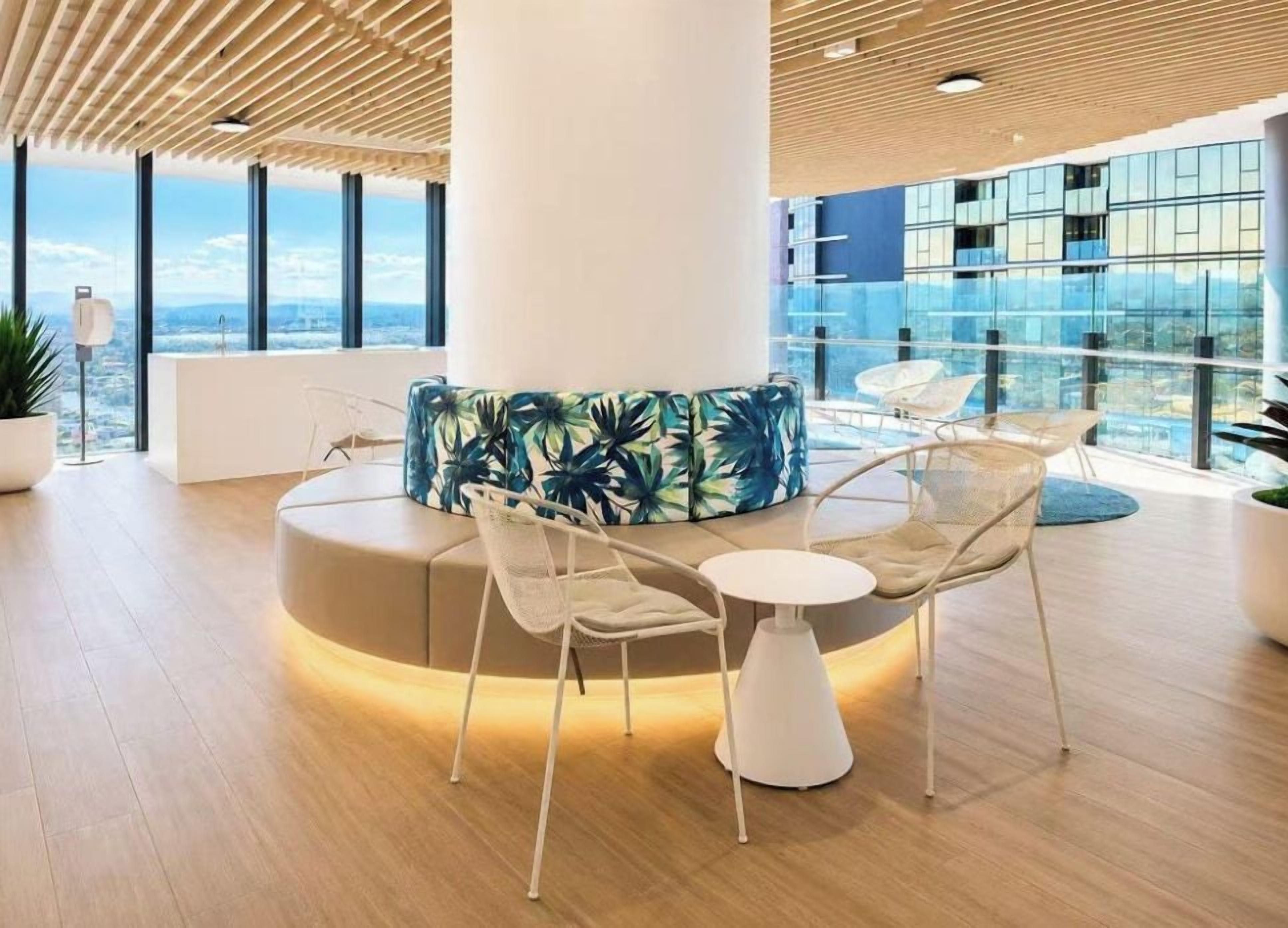 Un área de descanso moderna con un arreglo de asientos circulares, una mesa blanca y un ventanal con vista a la ciudad.