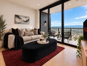 A modern living room with a sofa, a black ottoman, a red rug, and a large window offering a city view. - Brand NEW Lvl 45 Star Haven | Supercars & Views (Broadbeach)