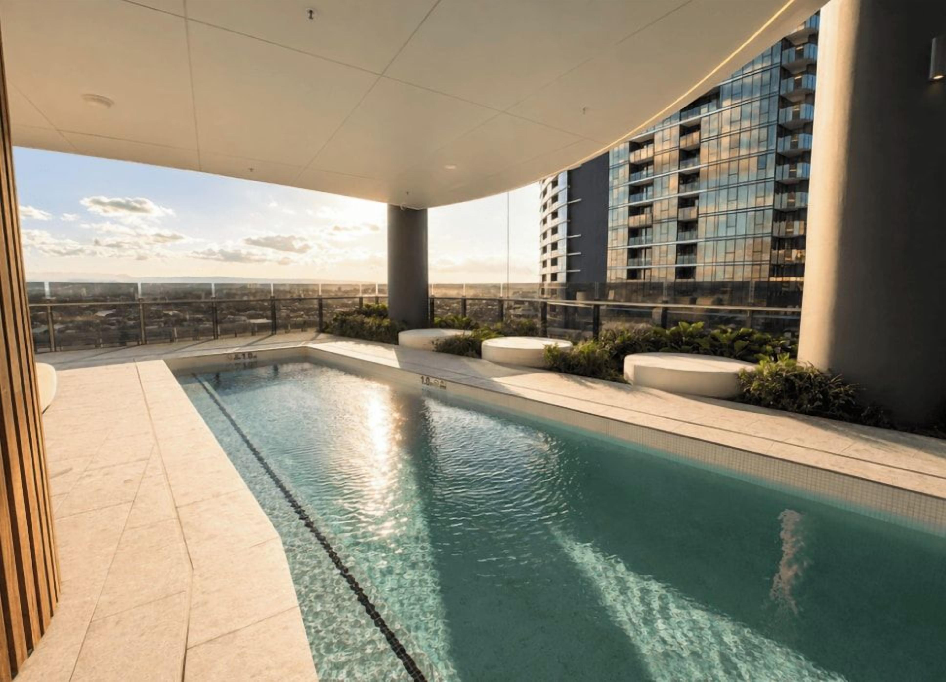 Una piscina en la azotea con vistas despejadas al paisaje urbano, rodeada de edificios modernos y una barandilla de cristal.