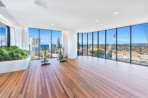 A spacious room with large windows offering a city view, a wooden floor, and exercise equipment. - Luxe 2BR @ The Star | Ocean+River Views, Pool, Gym (Broadbeach)