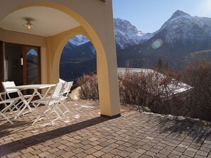 Ein Sitzbereich im Freien mit Tisch und Stühlen, eine Glastür und Blick auf die Berge.