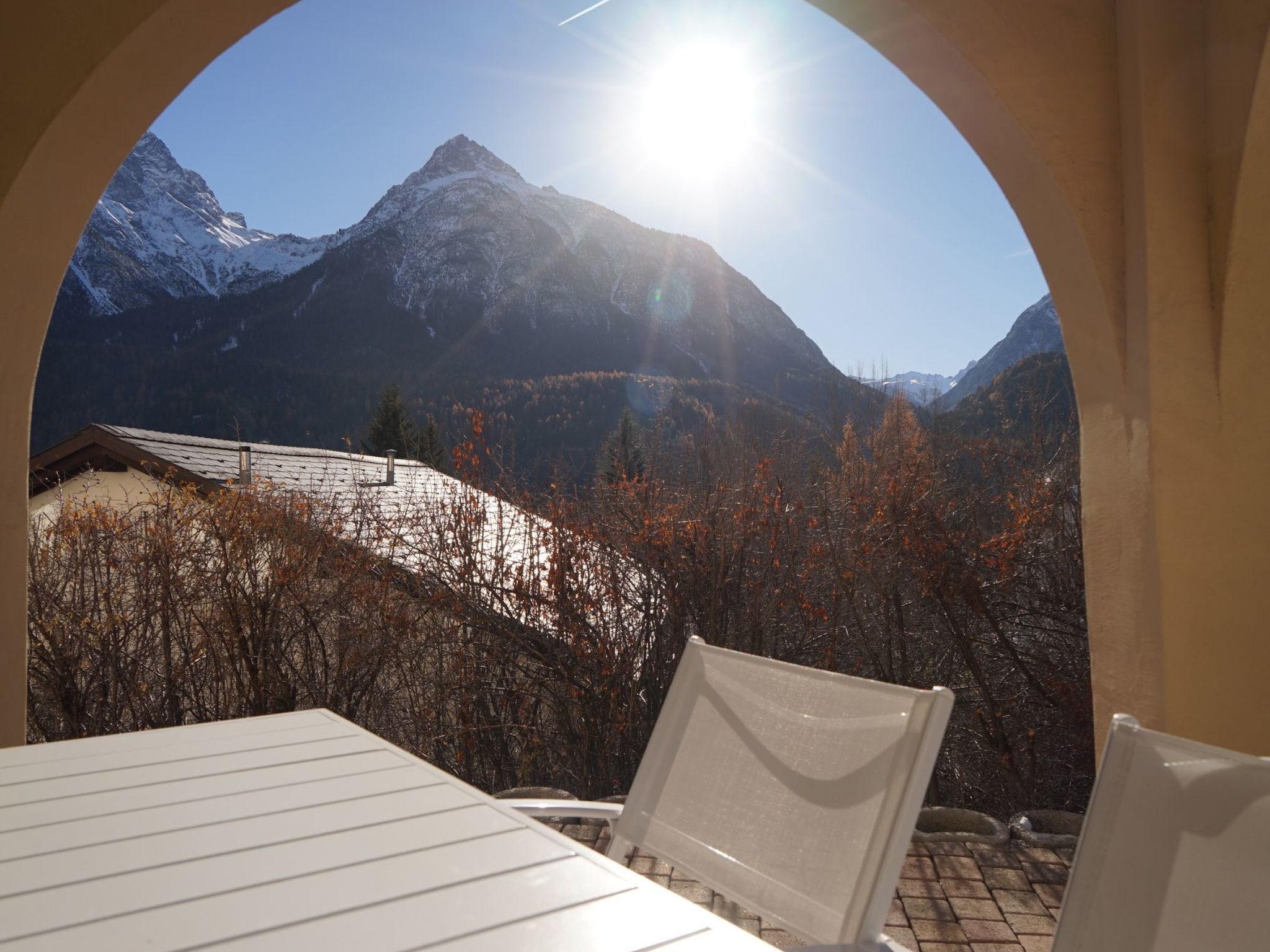 A dining area with a mountain view through an arched window, a table, and chairs.