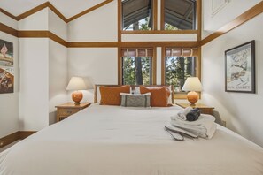 Ein Hotelzimmer mit einem großen Bett, zwei Nachttischen, einem Fenster mit Blick auf Bäume und einem Gemälde an der Wand.