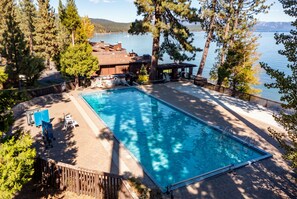 A rectangular swimming pool with a wooden deck, surrounded by trees and a view of a lake. - NEW Gated Tahoe City Ski Condo, Pier & Fireplace (Tahoe City)