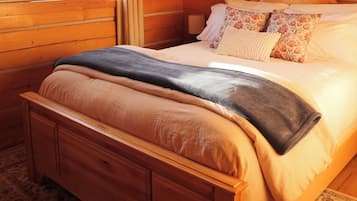 A wooden cabin bedroom with a bed, a window, and framed pictures on the wall.