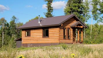 A log cabin with a gabled roof, a chimney, and a porch with a railing.