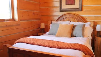 A wooden cabin room with a bed, two bedside tables, a window, and a framed picture on the wall.