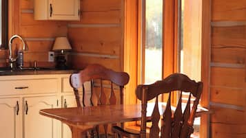 A wooden interior with a dining table and chairs, a chandelier, and a window with a view.