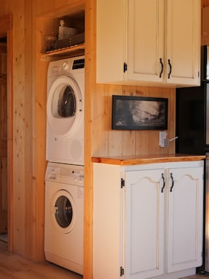 A compact laundry room with stacked washing machines, a flat-screen TV, and white cabinetry.