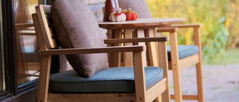 A wooden deck with two chairs and a table, a vase with dried plants, and a potted plant.