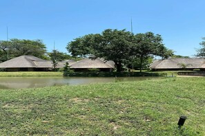 A grassy area with a pond, surrounded by thatched-roof structures. - Kruger Park Lodge Unit 81 (Mbombela)