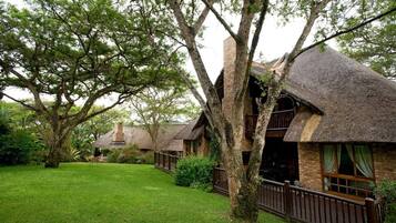 A rustic building with a thatched roof, surrounded by lush greenery and trees.