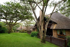 A rustic building with a thatched roof, surrounded by lush greenery and trees. - Kruger Park Lodge Unit 81 (Mbombela)