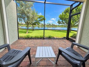 A patio with two chairs and a table, overlooking a lake with trees and a grassy area. - Lakeview Villa 2-bedroom 2 Bath plus den - pool! (Naples)